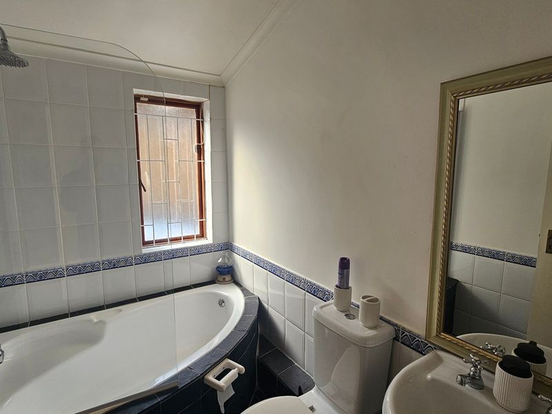 A functional bathroom featuring a corner bathtub with shower attachment, pedestal basin, and wall-mounted mirror, finished with classic tiled splashbacks.