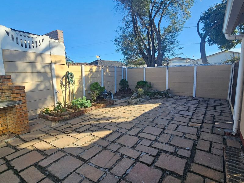 A paved outdoor patio area featuring a built-in brick braai, enclosed by a precast boundary wall with electric fencing.