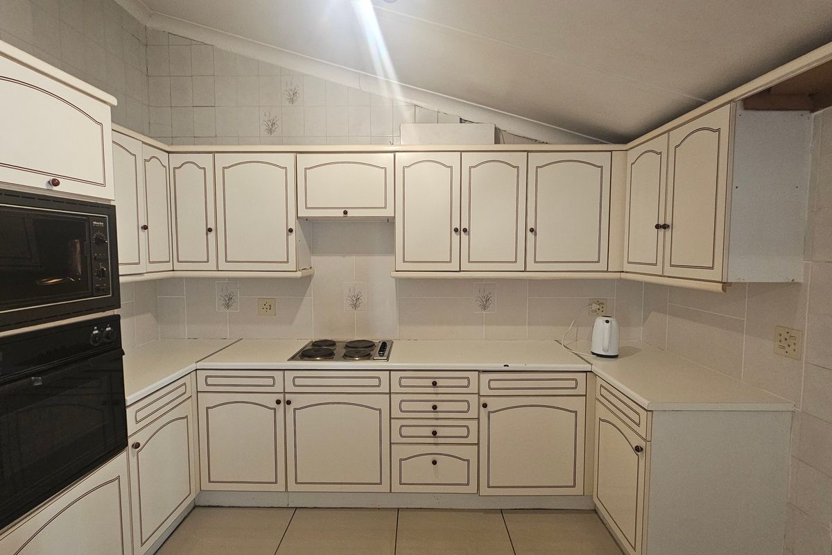 A functional kitchen featuring built-in oven, microwave, electric hob, and tiled splashbacks with ample cabinetry storage.