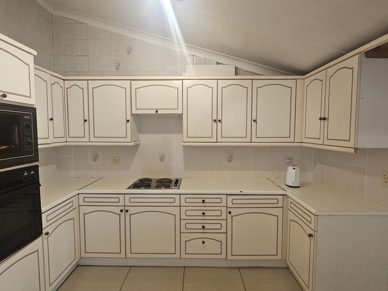 A functional kitchen featuring built-in oven, microwave, electric hob, and tiled splashbacks with ample cabinetry storage.