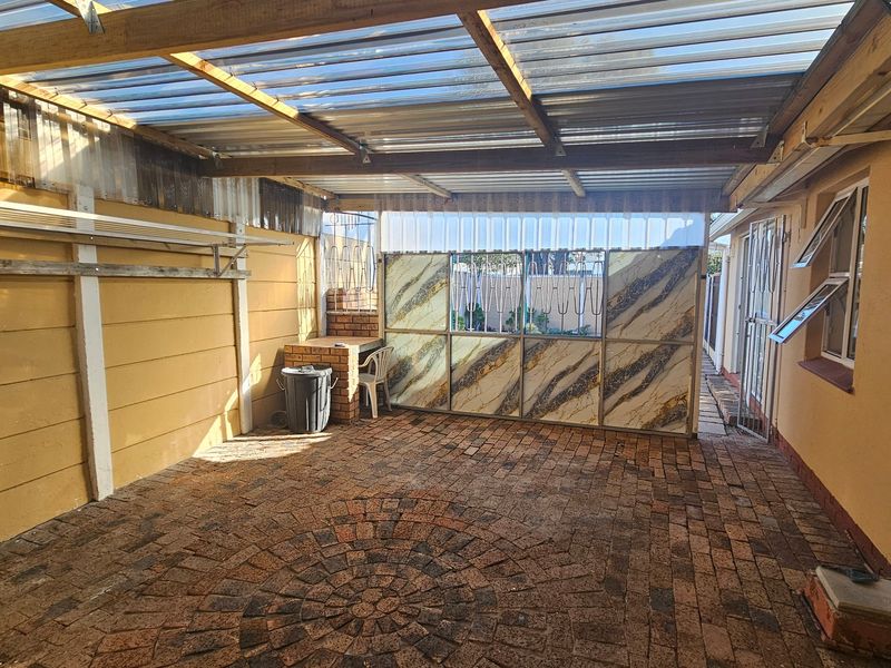 Covered outdoor patio area featuring brick paving, a built-in brick braai, and a translucent corrugated roof structure.