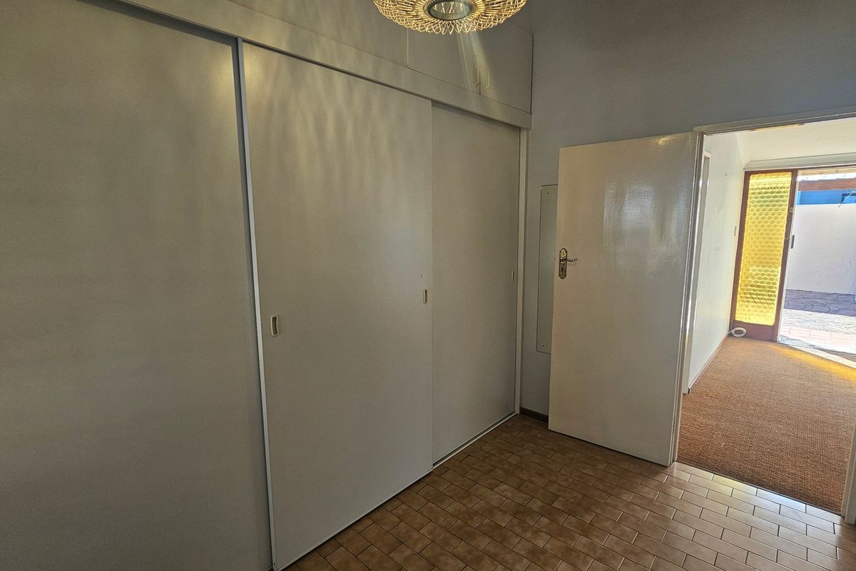 A vacant bedroom featuring built-in sliding door cupboards and tiled flooring, providing a clean canvas for potential updates.