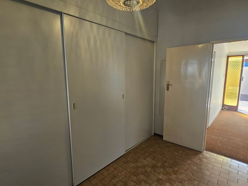 A vacant bedroom featuring built-in sliding door cupboards and tiled flooring, providing a clean canvas for potential updates.