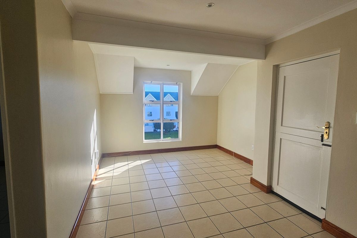 A bright, empty bedroom featuring neutral walls, tiled flooring, and a window providing natural light.