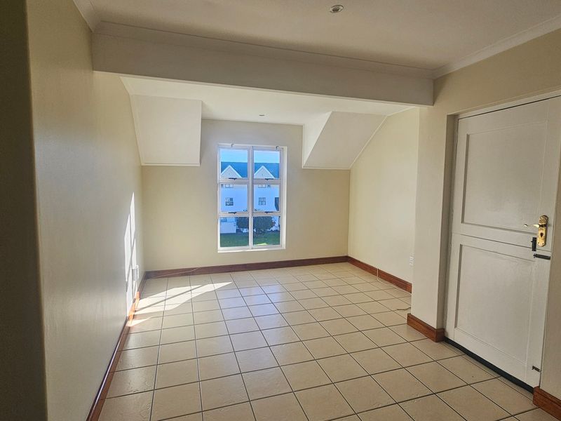 A bright, empty bedroom featuring neutral walls, tiled flooring, and a window providing natural light.