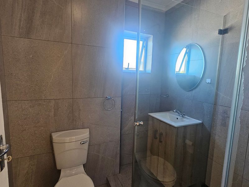 Modern bathroom featuring full-height wall tiling, a vanity cabinet with integrated basin, and a glass-enclosed shower area.