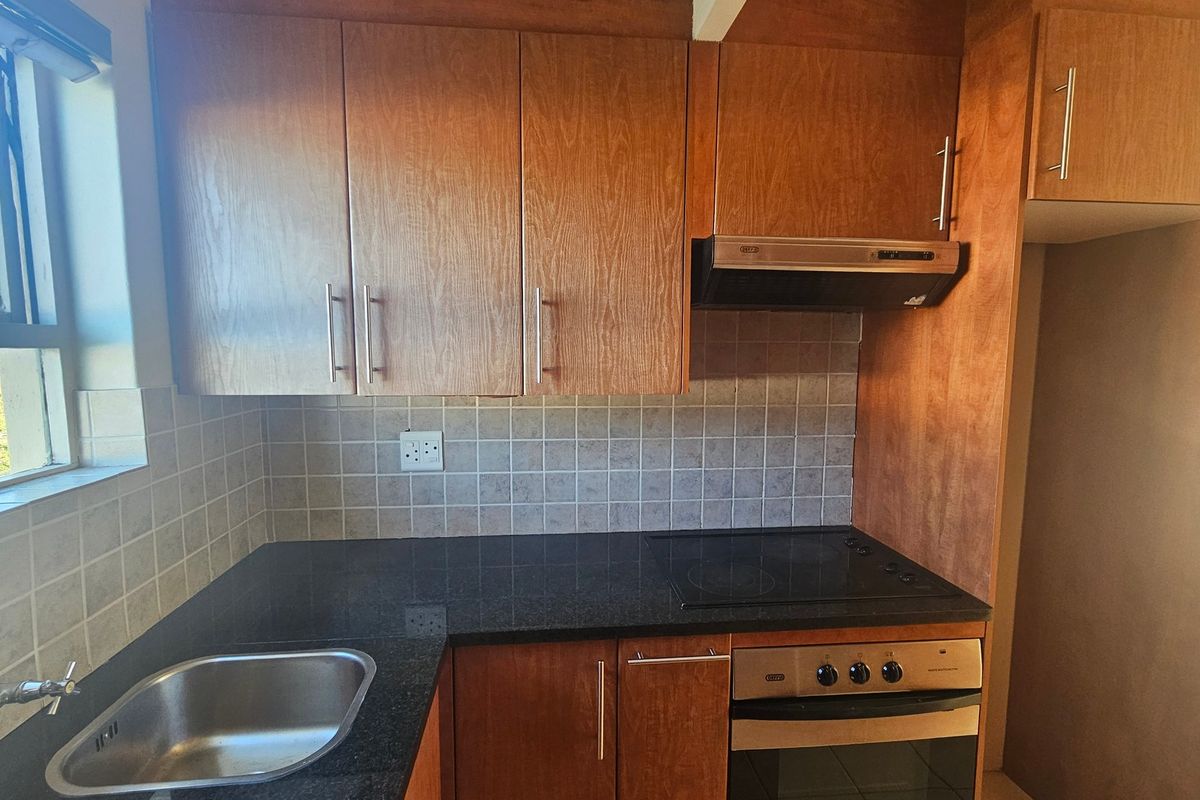 A functional kitchen featuring wooden cabinetry, granite countertops, a built-in oven with hob, extractor fan, and a stainless steel sink.