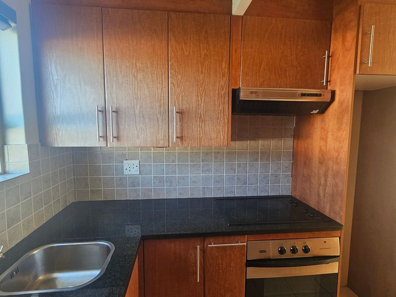 A functional kitchen featuring wooden cabinetry, granite countertops, a built-in oven with hob, extractor fan, and a stainless steel sink.