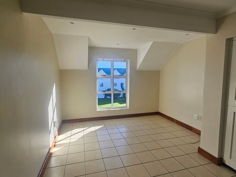 A bright, empty bedroom featuring tiled flooring, recessed ceiling lights, and a window with a view of the surrounding complex.