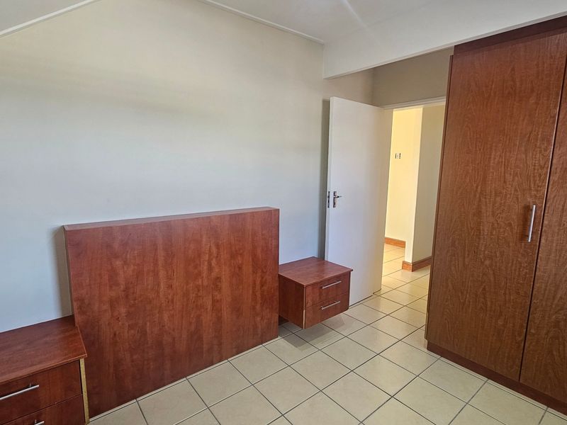 A bedroom featuring built-in wooden cupboards, a matching built-in headboard with bedside tables, and neutral tiled flooring.