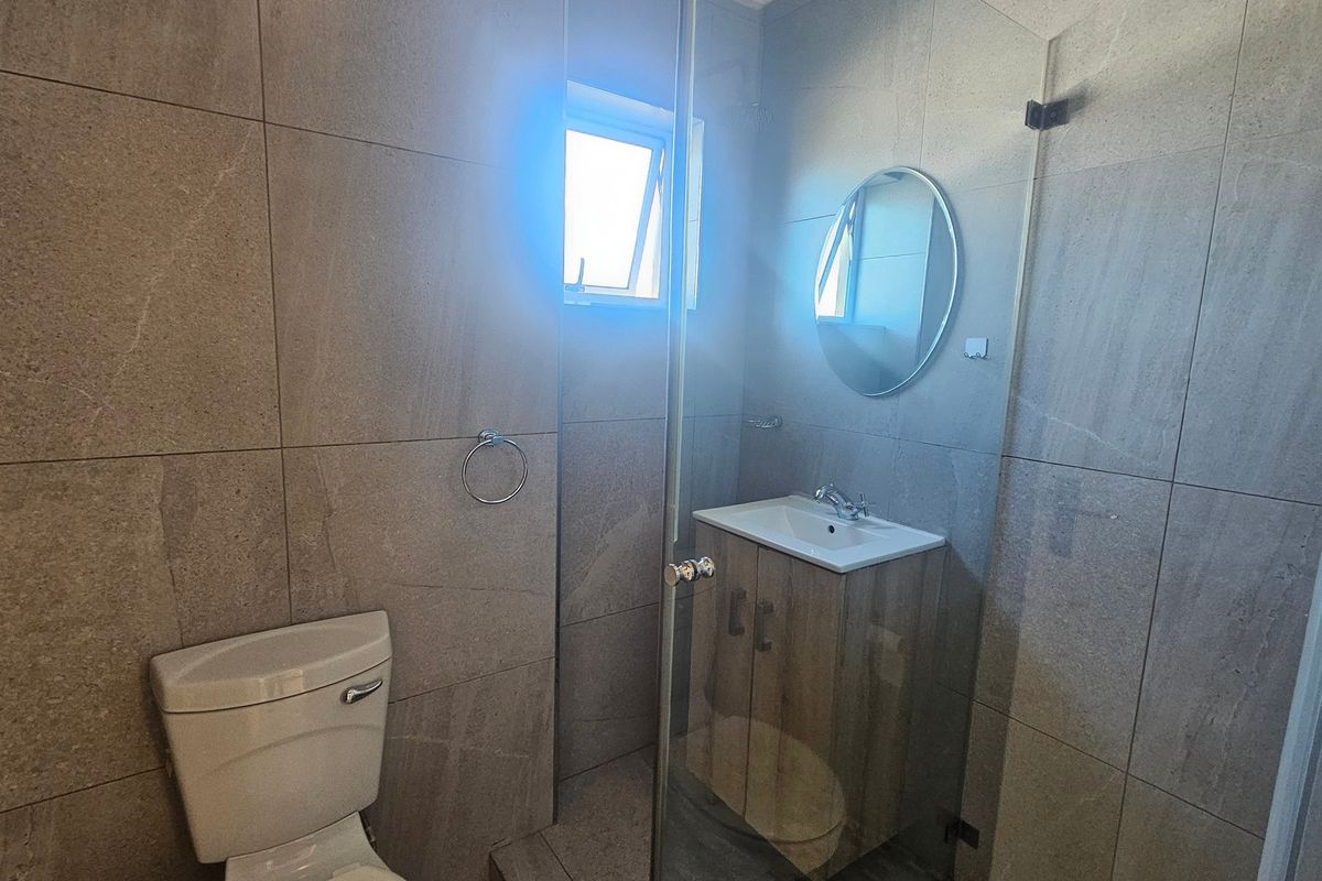 Modern bathroom featuring floor-to-ceiling stone-look tiles, a vanity cabinet with basin, and a glass-enclosed shower area.