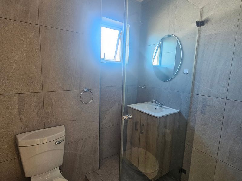 Modern bathroom featuring floor-to-ceiling stone-look tiles, a vanity cabinet with basin, and a glass-enclosed shower area.