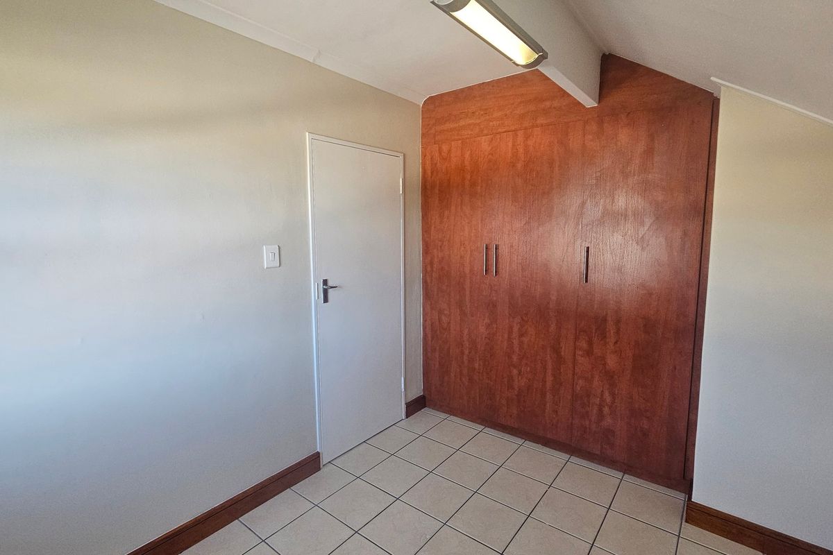A clean, empty bedroom featuring tiled flooring and ample built-in wooden cupboard storage space.