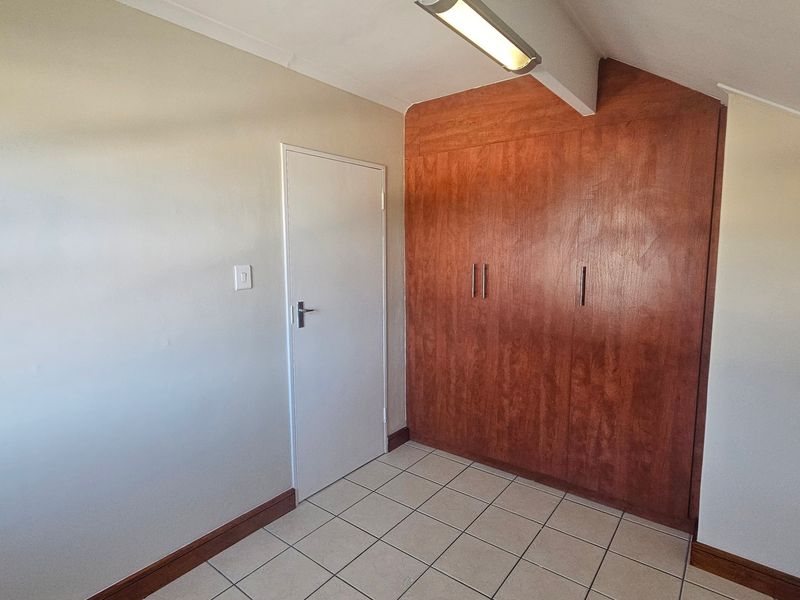 A clean, empty bedroom featuring tiled flooring and ample built-in wooden cupboard storage space.
