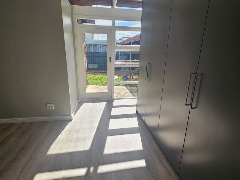 A bright, empty bedroom featuring modern laminate flooring, floor-to-ceiling built-in cupboards, and a glass-paneled door providing direct access to the rear garden.