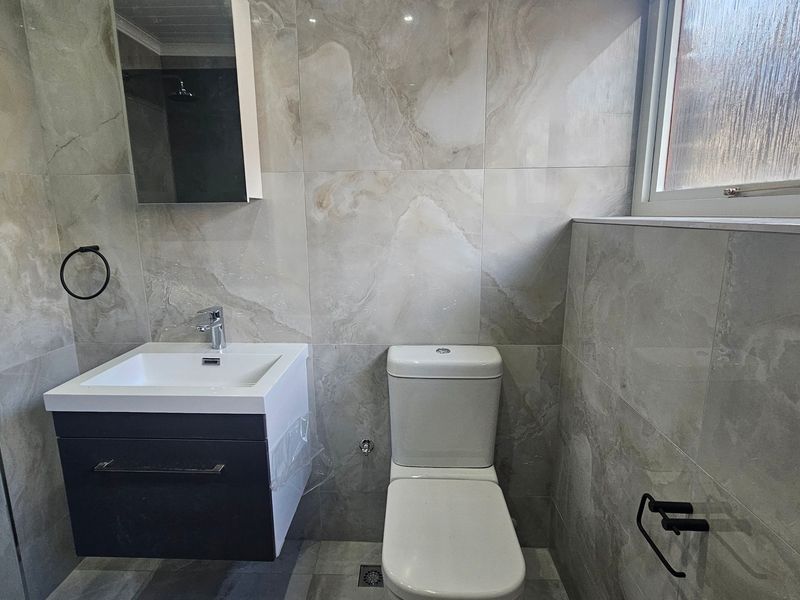 Modern bathroom featuring floor-to-ceiling marble-look tiling, a wall-mounted vanity with basin, and a contemporary toilet suite.