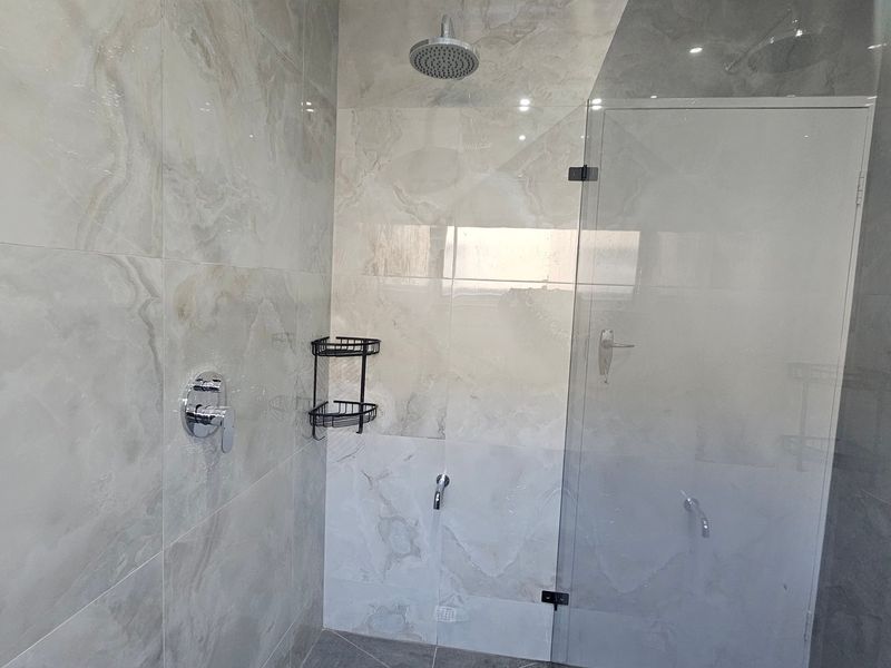 Modern walk-in shower featuring large-format polished porcelain wall tiles, a rainfall shower head, and a frameless glass screen.