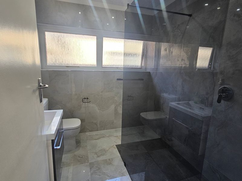 Modern bathroom featuring a walk-in shower with glass screen, vanity cabinet, toilet, and contemporary floor-to-ceiling tiling.