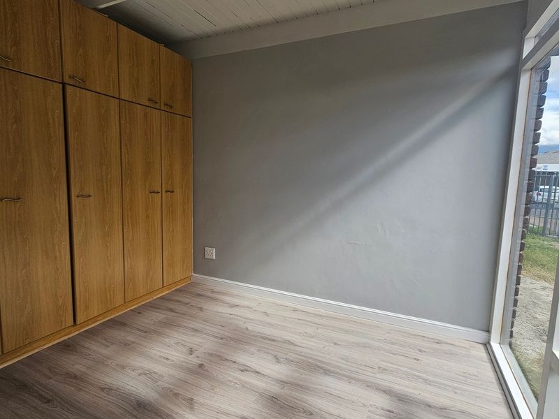 A bright, empty bedroom featuring light wood-look laminate flooring and extensive built-in wooden cupboards, offering a clean and neutral space.