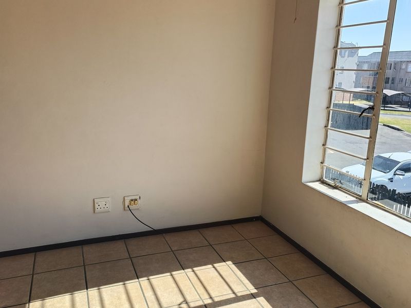 An empty bedroom featuring tiled flooring, large windows with security bars, and neutral wall finishes, offering a blank canvas for personalization.
