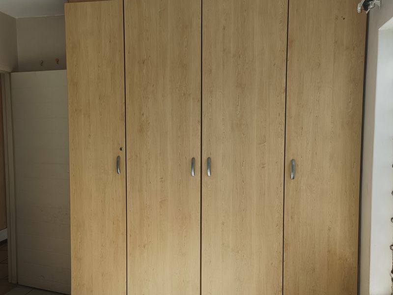 A bedroom featuring light wood-finish built-in cupboards and a window fitted with security bars.