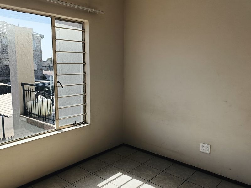 An empty bedroom featuring tiled flooring, security bars on the window, and neutral wall finishes, ready for personalization.