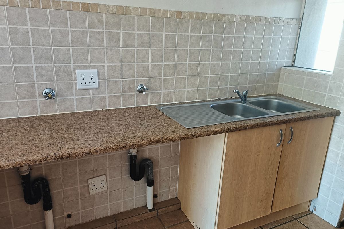 A functional kitchen area featuring a granite countertop, double bowl stainless steel sink, and tiled splashback with integrated plumbing and electrical points.