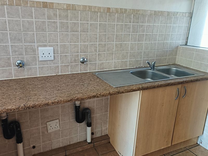 A functional kitchen area featuring a granite countertop, double bowl stainless steel sink, and tiled splashback with integrated plumbing and electrical points.