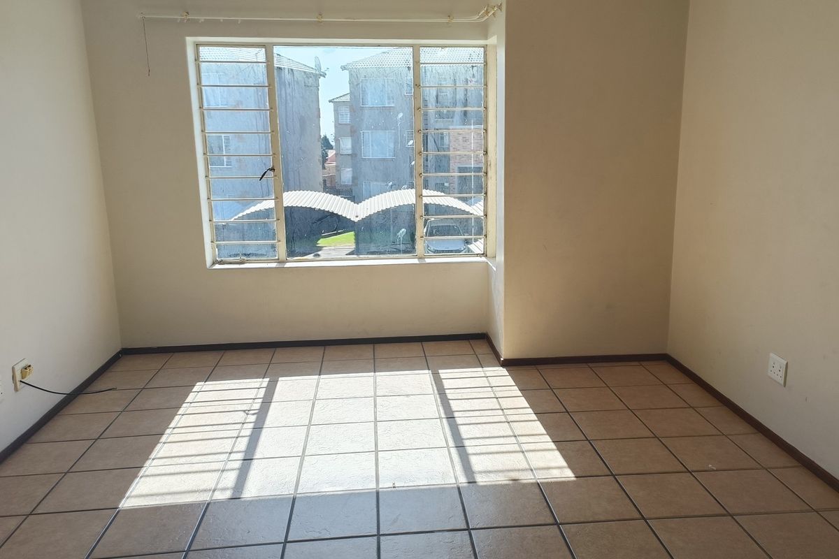 An empty living room featuring tiled flooring, a large window with security bars, and neutral wall finishes, offering a blank canvas for personalization.