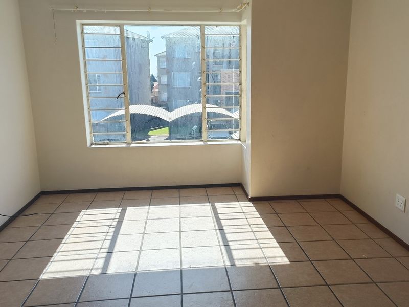 An empty living room featuring tiled flooring, a large window with security bars, and neutral wall finishes, offering a blank canvas for personalization.