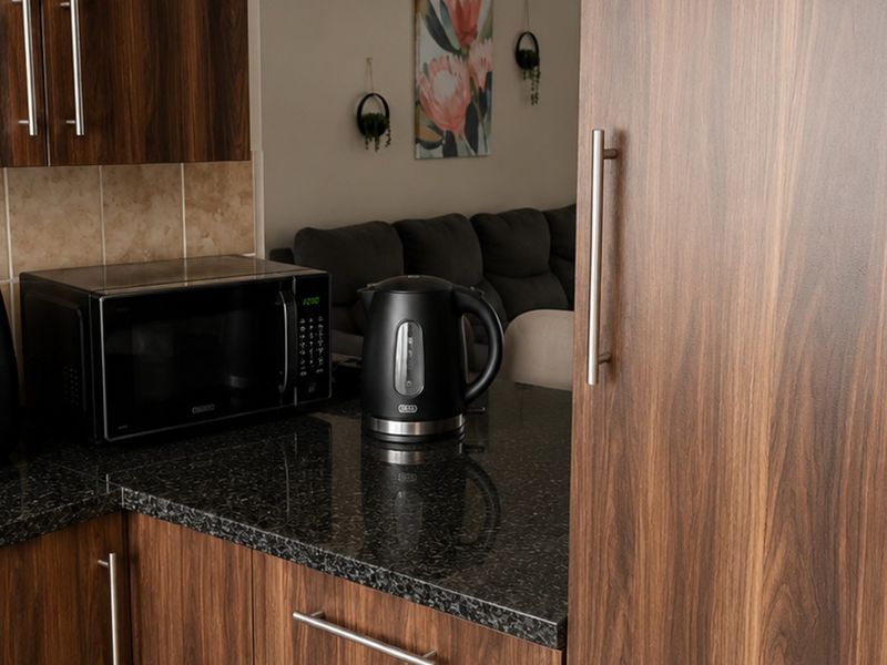 A modern kitchen area featuring dark wood-look laminate cabinetry, a polished granite countertop, and a neutral tiled backsplash.