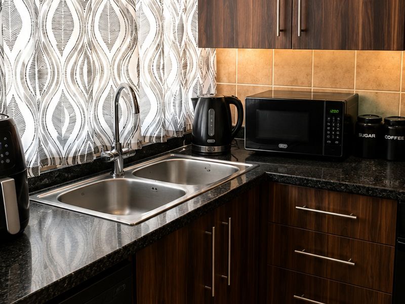 A well-maintained kitchen featuring dark wood cabinetry, granite countertops, a double basin sink, and integrated appliances with under-cabinet lighting.