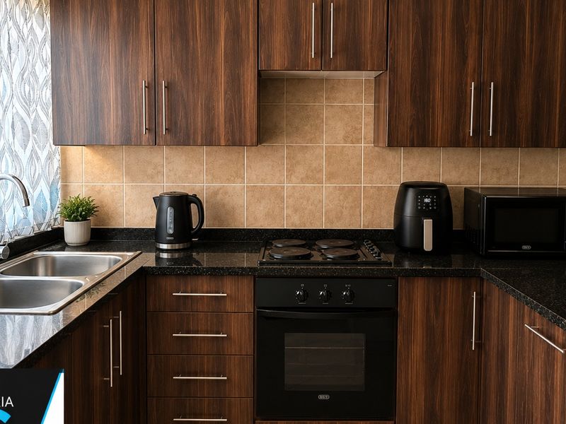 A well-maintained kitchen featuring dark wood cabinetry, granite countertops, a double bowl stainless steel sink, and integrated oven with electric hob.