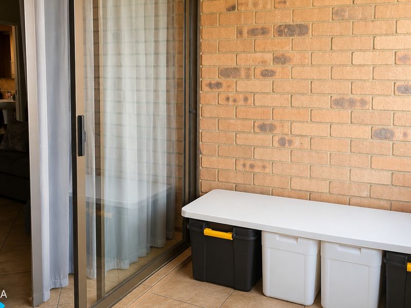 A covered balcony featuring exposed brick walls, tiled flooring, and a sliding glass door providing access to the interior living space.