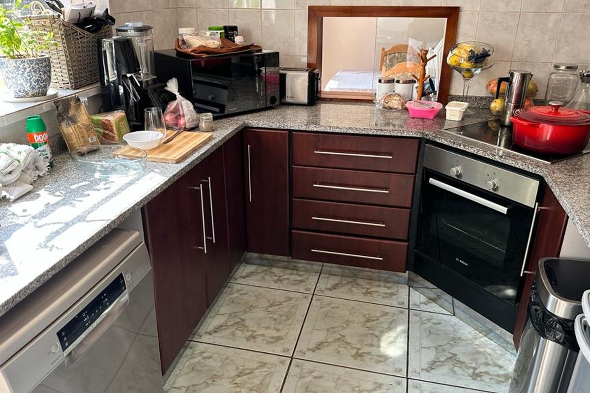 A functional kitchen featuring dark wood cabinetry, granite countertops, a built-in oven, and a ceramic hob with tiled backsplash and flooring.