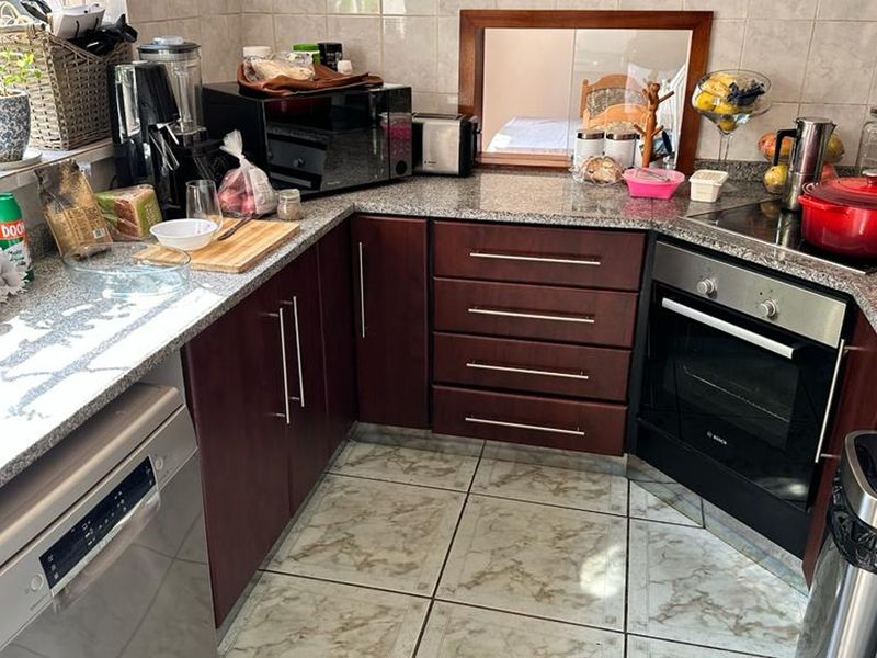 A functional kitchen featuring dark wood cabinetry, granite countertops, a built-in oven, and a ceramic hob with tiled backsplash and flooring.