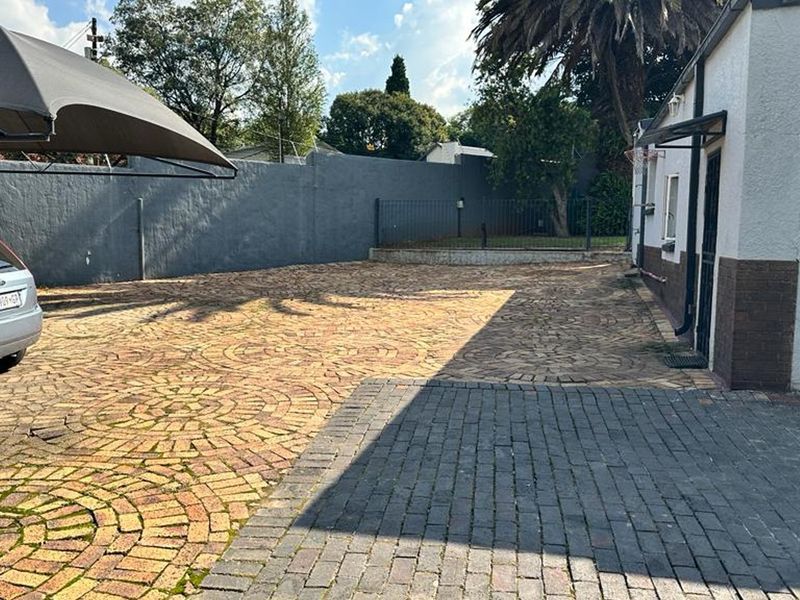 A paved front driveway area featuring a shade sail, boundary wall, and direct access to the main building structure.
