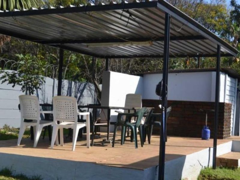 An outdoor patio area featuring a raised concrete platform covered by a corrugated metal roof structure with metal support posts.