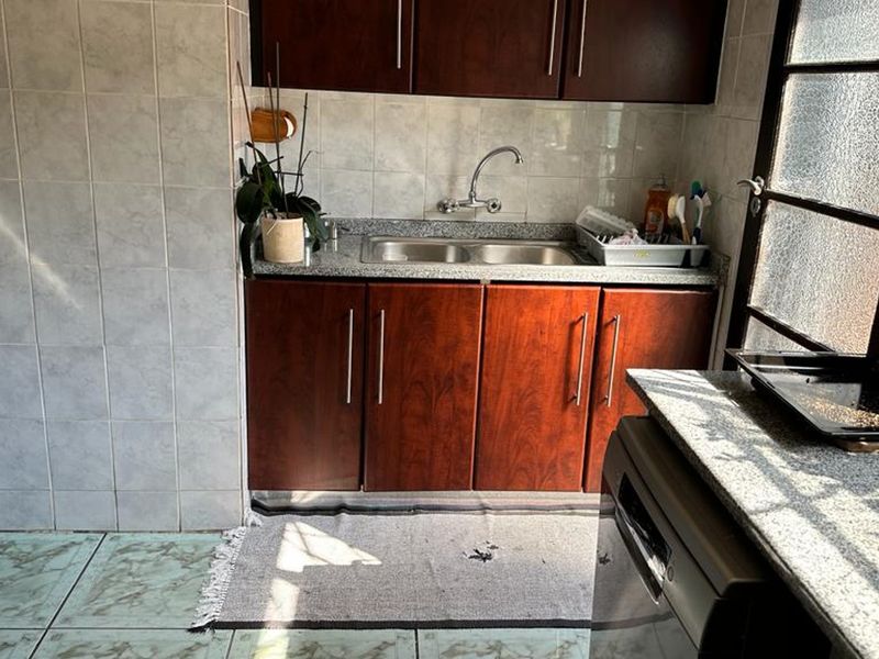A functional scullery area featuring dark wood cabinetry, granite countertops, and a double bowl sink with tiled wall finishes.