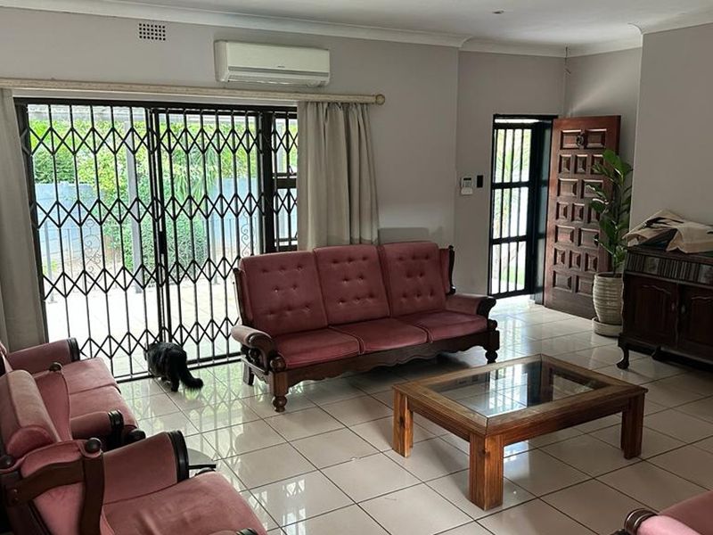 Spacious living room featuring neutral tiled flooring, a wall-mounted air conditioning unit, and direct access to the outdoor area through a secure sliding door.