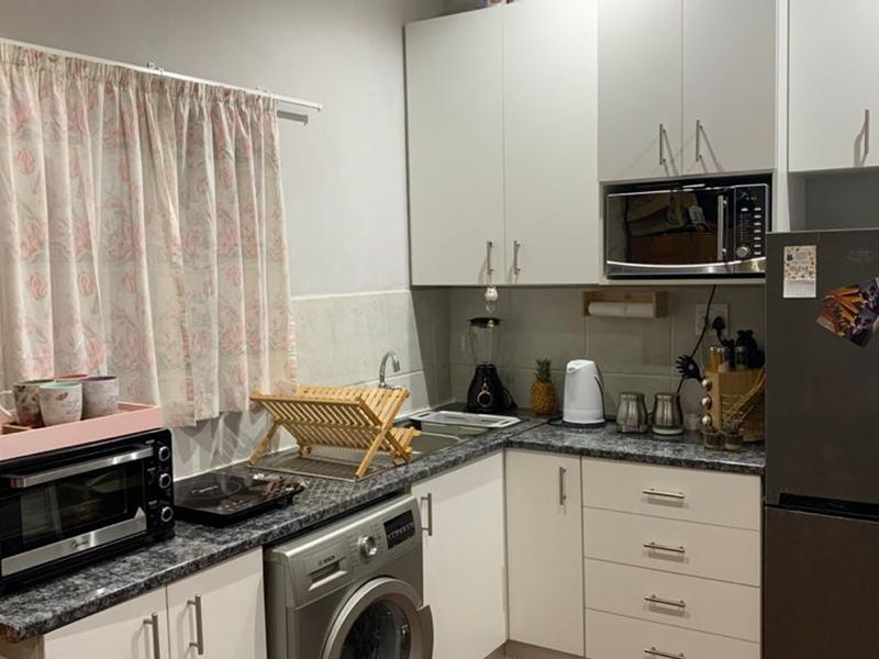 Compact kitchen featuring white cabinetry, laminate countertops, a stainless steel sink, and a built-in microwave with space for a washing machine.