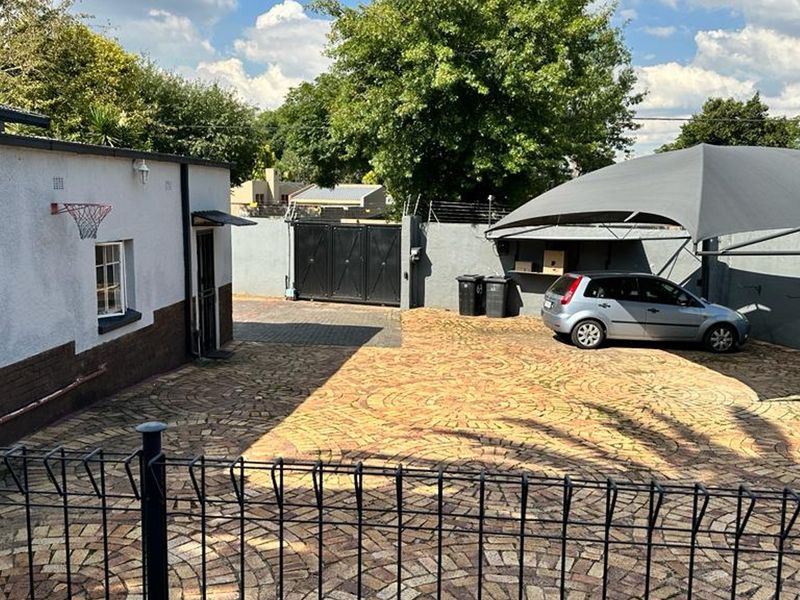 A paved front driveway featuring a shade sail carport, secure perimeter walling, and an electric gate entrance.