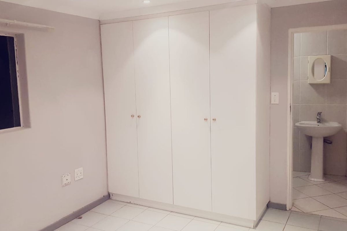A clean bedroom featuring built-in wardrobes, tiled flooring, and an en-suite bathroom with a pedestal basin.