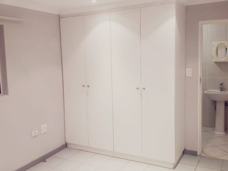 A clean bedroom featuring built-in wardrobes, tiled flooring, and an en-suite bathroom with a pedestal basin.