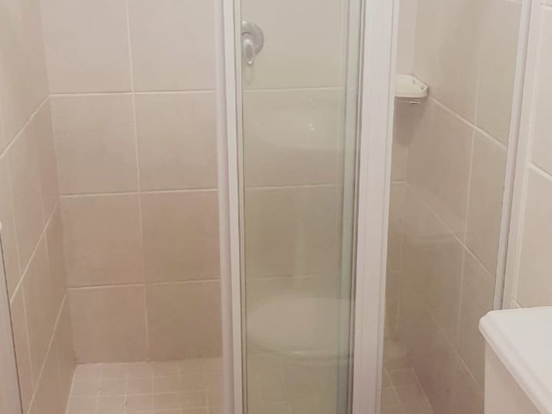 A functional bathroom featuring a shower enclosure with tiled walls and floor, including a standard toilet and wall-mounted towel rail.