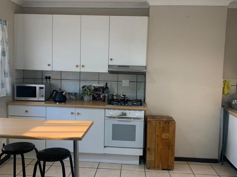 A functional kitchen featuring white cabinetry, a gas hob with extractor fan, tiled backsplash, and tiled flooring, providing a practical workspace.
