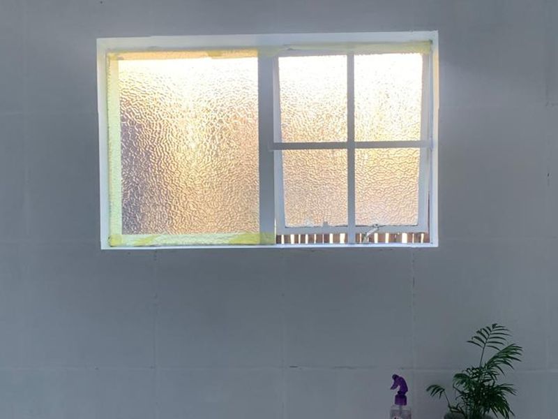 A close-up view of a window with textured glass, showing signs of ongoing maintenance or unfinished painting work around the frame.