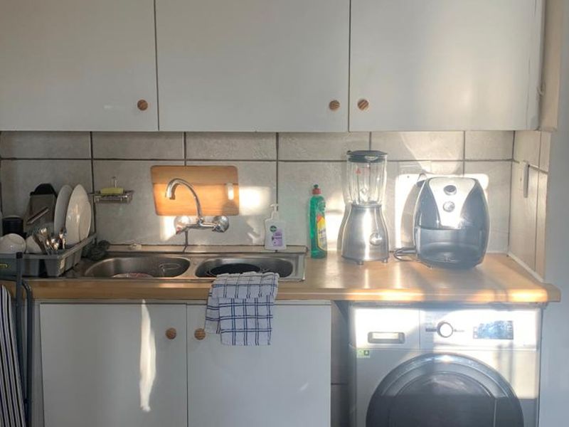 Compact kitchen area featuring white cabinetry, a double bowl stainless steel sink, tiled backsplash, and an integrated washing machine.