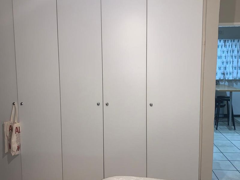 A bedroom featuring a large, white built-in wardrobe with simple hardware, providing ample storage space.