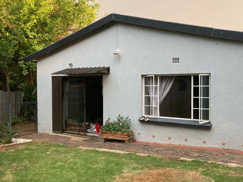 Rear view of the cottage featuring a sliding glass door, casement windows, and a brick paved walkway leading to the garden area.